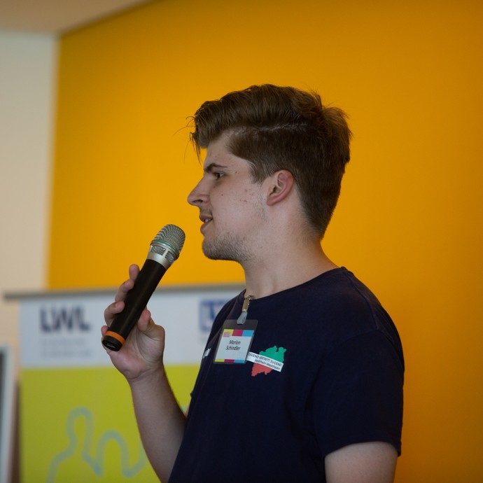 Das Bild zeigt einen jungen mit Mikro auf der Bühne (vergrößerte Bildansicht wird geöffnet)