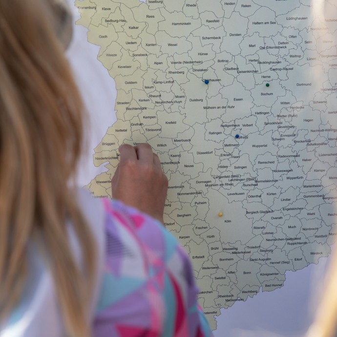Das Bild zeigt ein Kind von hinten, das eine Pinn-Nadel in eine Landkarte steckt (öffnet vergrößerte Bildansicht)