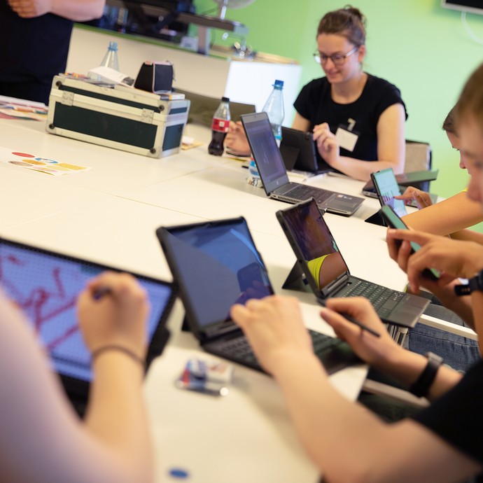 Das Bild zeigt junge Menschen, die an Tablets arbeiten (vergrößerte Bildansicht wird geöffnet)