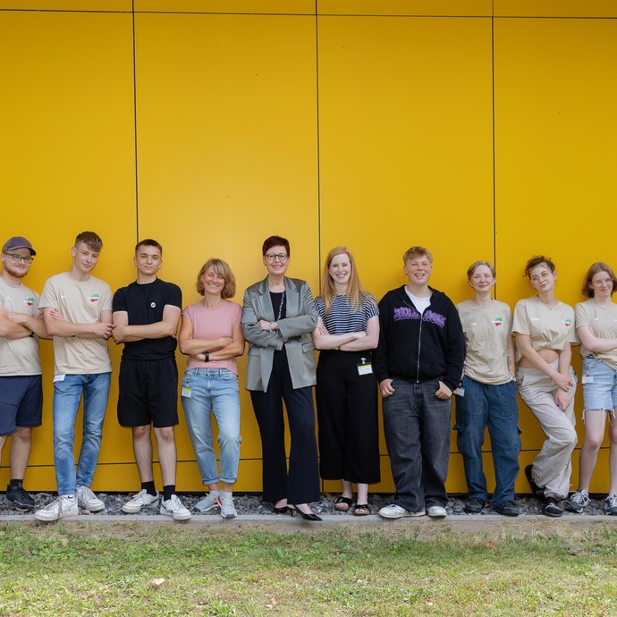 Das Bild zeigt die JvJ-Mitglieder, Frau Westers, Anna Richters und Inga Abels, die vor einer gelben Wand stehen. Sie lachen in die Kamera (vergrößerte Bildansicht wird geöffnet)