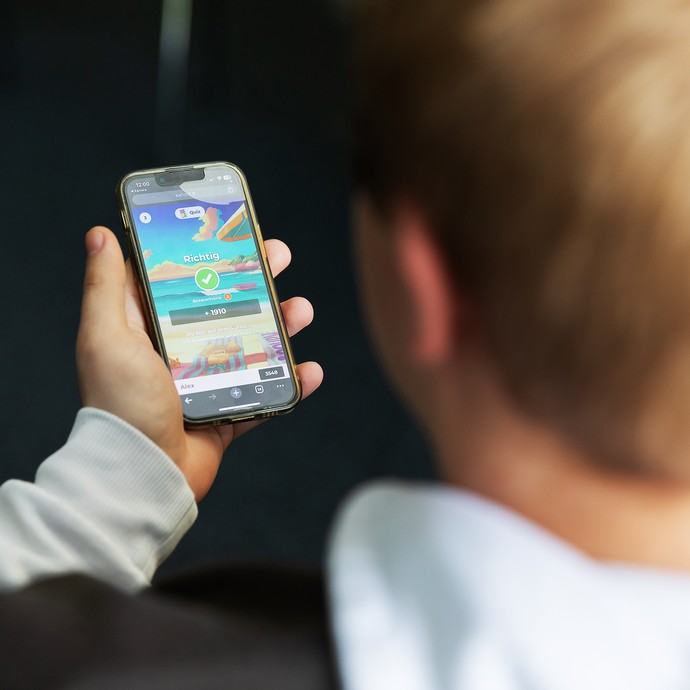 Das Bild zeigt ein Kind, das auf ein Smartphone-Display schaut (vergrößerte Bildansicht wird geöffnet)