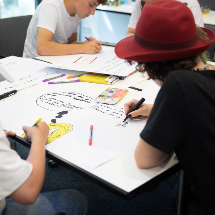 Das Bild zeigt junge Menschen an einem Tisch, die malen (vergrößerte Bildansicht wird geöffnet)