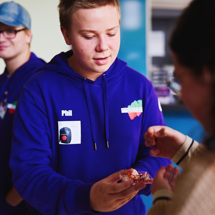 Ein Jugendlicher von JvJ NRW verteilt Stecknadeln, damit die Teilnehmenden auf der NRW-Karte eintragen können, woher sie kommen. (vergrößerte Bildansicht wird geöffnet)