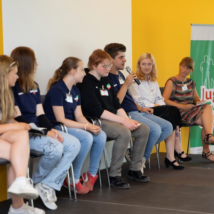 Das Bild zeigt Mitglieder von Jugend vertritt Jugend mit Mikro auf der Bühne (vergrößerte Bildansicht wird geöffnet)