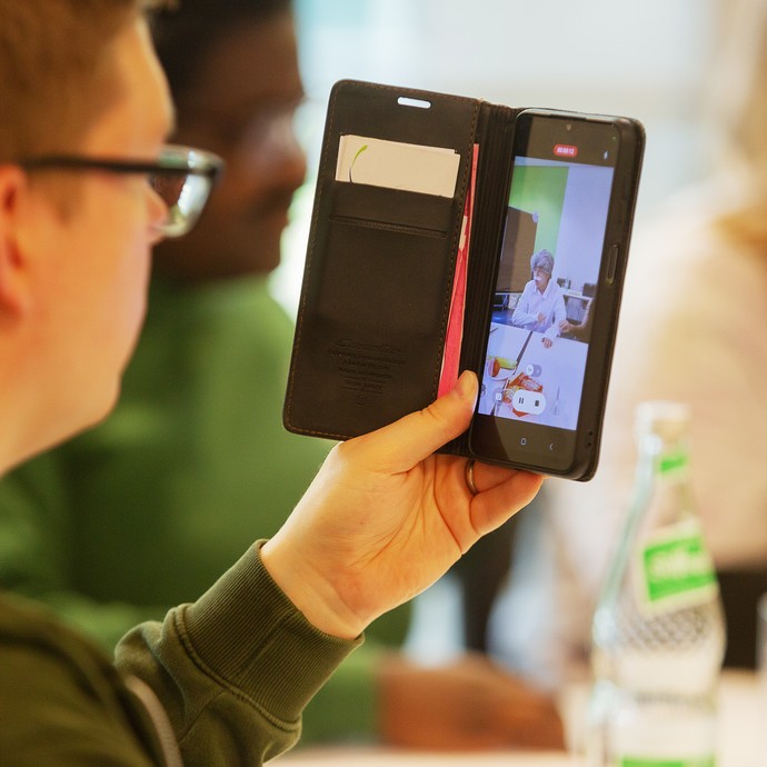 Das Bild zeigt eine Person, die eine Szene mit dem Smartphone filmt (vergrößerte Bildansicht wird geöffnet)