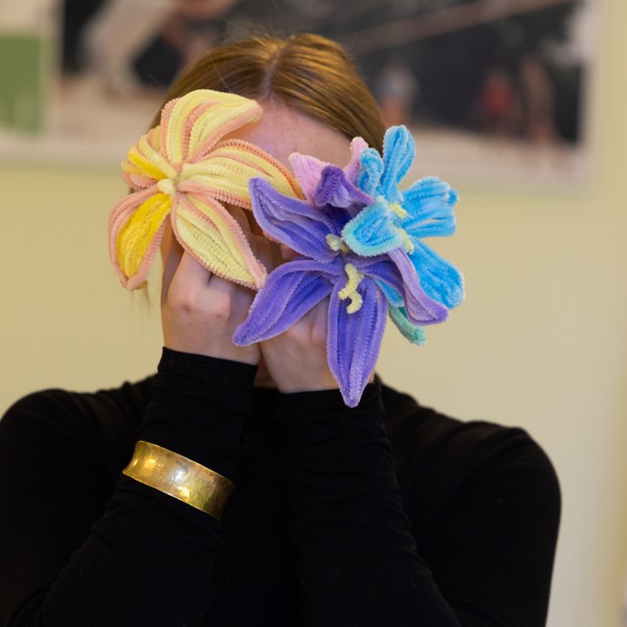 Eine Person hält sich zwei gebastelte Blumen vor ihr Gesicht. (vergrößerte Bildansicht wird geöffnet)