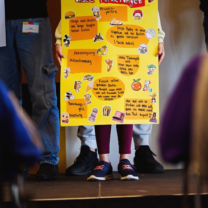Ein Mädchen hält auf der Bühne ein Plakat mit "Unseren Forderungen". (vergrößerte Bildansicht wird geöffnet)